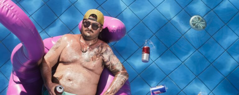 Homem a boiar numa piscina com latas de cerveja à volta